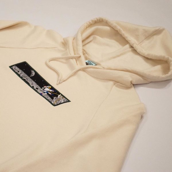 cream colored hoody featuring embroidery of astronaught climbing on the moon