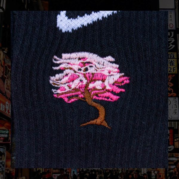 Steinblokk - Black crew sock with a pink and brown embroidery of a cherry blossom tree. The photo was taken under the glow of sunset with a wood background.