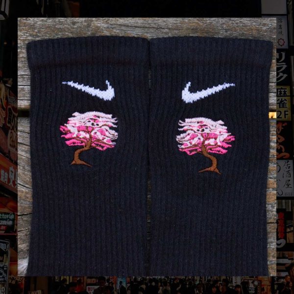 Steinblokk - Black crew sock with a pink and brown embroidery of a cherry blossom tree. The photo was taken under the glow of sunset with a wood background.