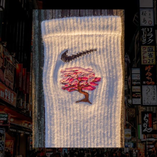 Steinblokk - White crew sock with a pink and brown embroidery of a cherry blossom tree. The photo was taken under the glow of sunset with a wood background.