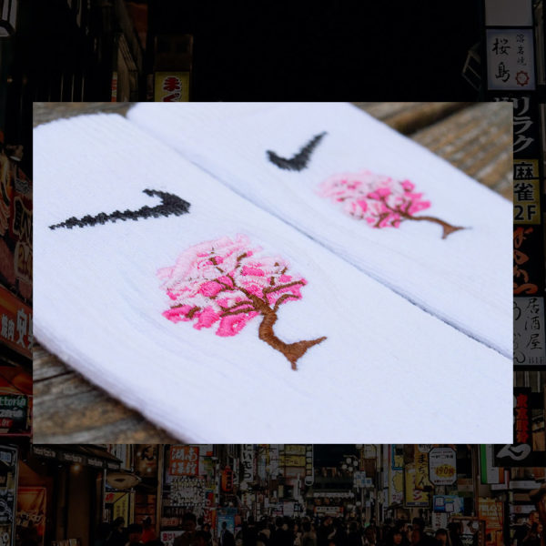 Steinblokk - White crew sock with a pink and brown embroidery of a cherry blossom tree. The photo was taken under the glow of sunset with a wood background.